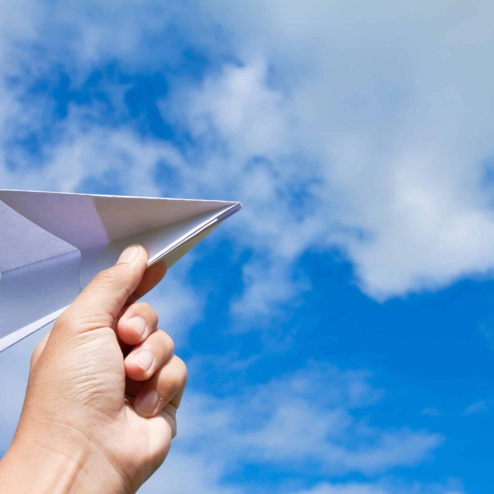 plane in hand hand with paper plane against blue sky